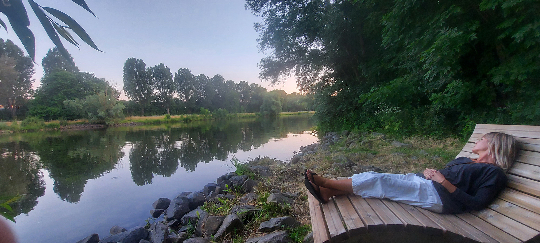 A person sitting on a bench by a river

Description automatically generated